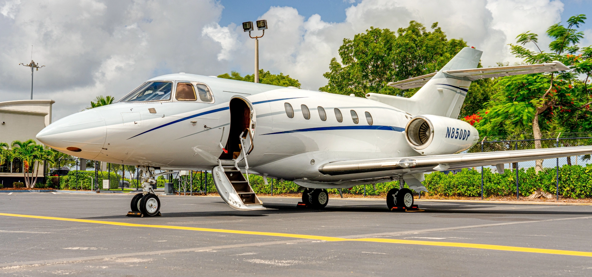 A small private jet is parked on an airport tarmac, open door inviting, under outdoor lighting. Trees and cloudy skies are in the background, setting a serene stage for those exploring luxury jet sales or seeking expert aviation consulting services.