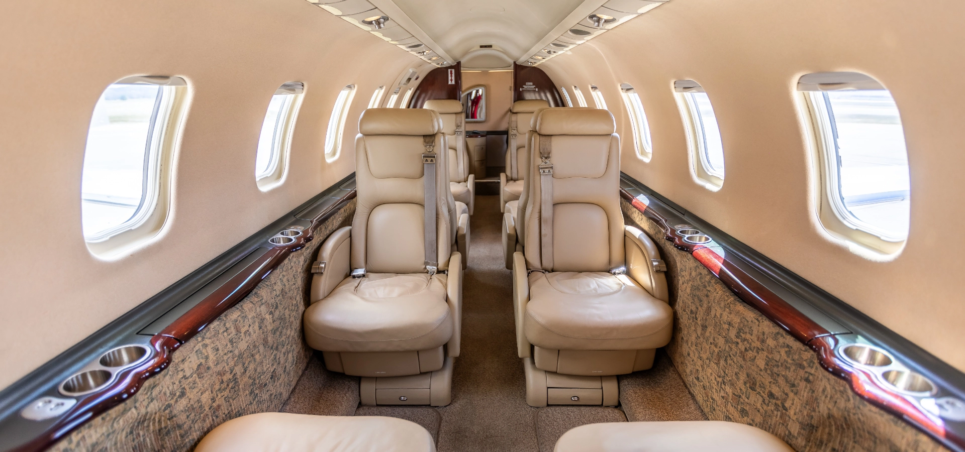 The interior of this business jet for sale features beige leather seats and elegant wooden paneling, showcasing two rows of facing seats across a narrow aisle.