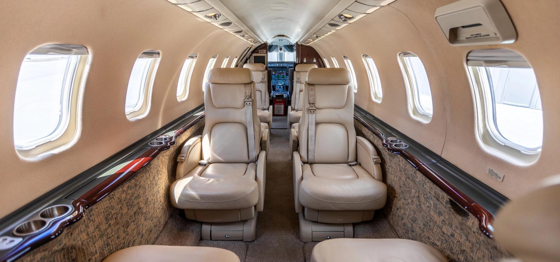 Experience the luxurious interior of a private jet, featuring beige leather seats, side windows, and overhead storage compartments. Explore our exclusive business jets for sale to elevate your travel in unparalleled comfort.