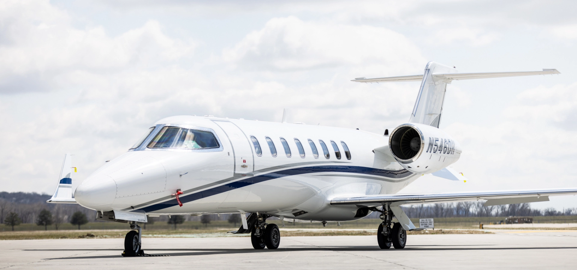 A white private jet, symbolizing the pinnacle of luxury jet sales, is parked on an airport runway under a cloudy sky.