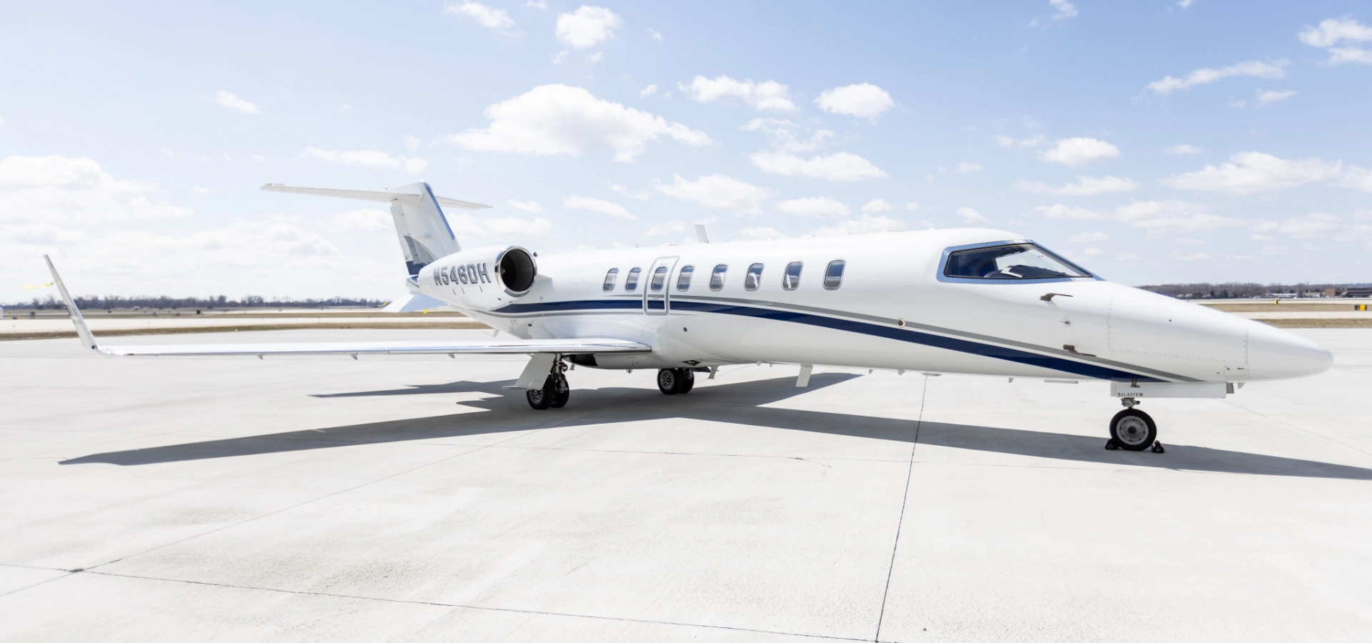 A sleek white private jet, symbolizing luxury and business prowess, is parked on the sunlit airport tarmac under a clear blue sky, exemplifying corporate jet sales at their finest.
