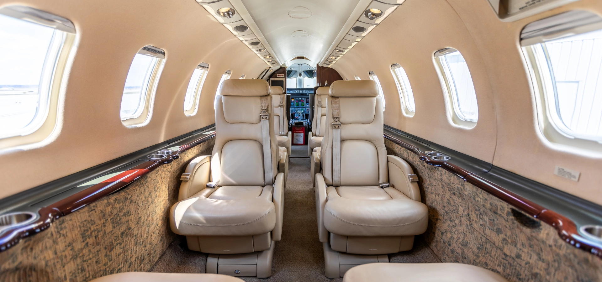 Interior view of a private jet showcases beige leather seats in two rows, windows lining both sides, and a cockpit at the front—perfect for those considering aircraft acquisition or exploring top business jets for sale through our aviation consulting services.