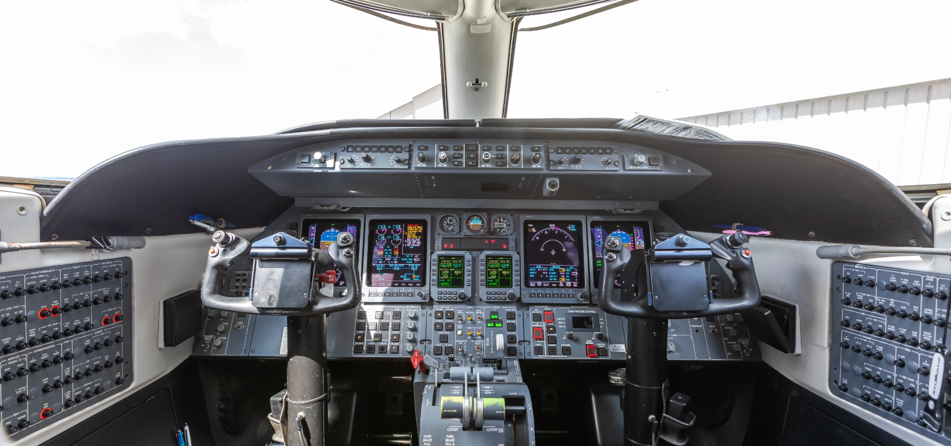 The cockpit of an aircraft, often found in luxury jet sales, features multiple control panels, gauges, and two joysticks.