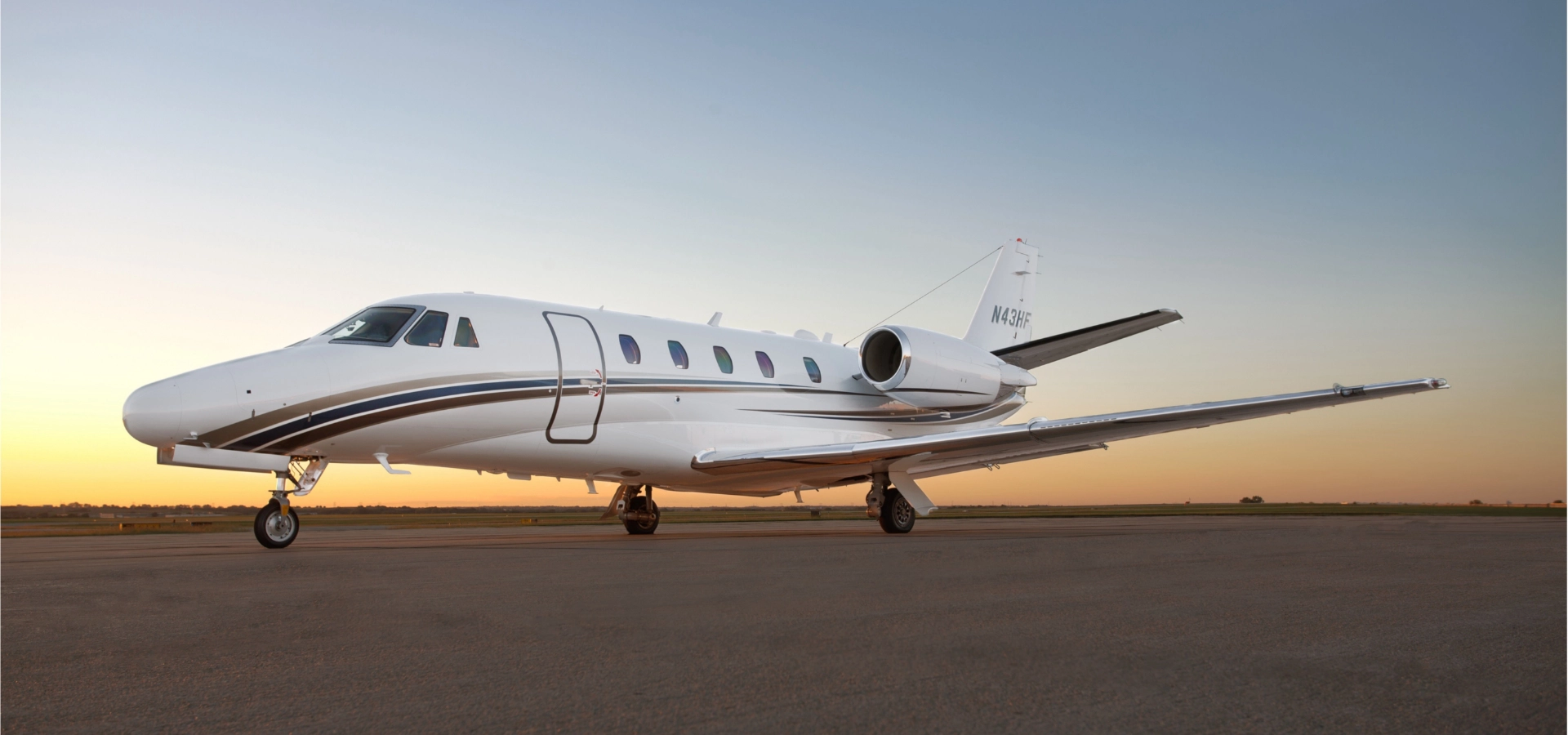 A sleek white private jet is parked on a tarmac with a breathtaking sunset in the background.