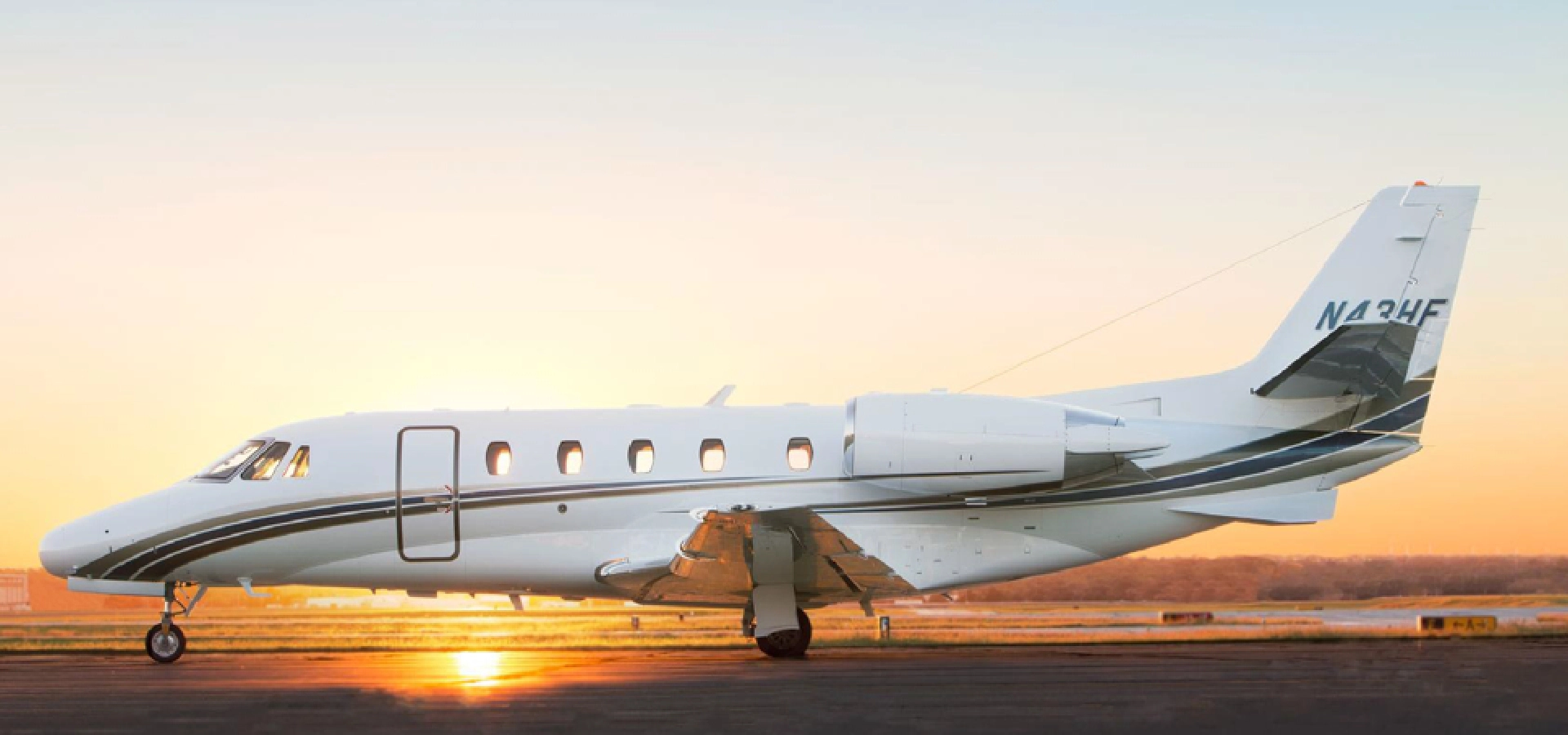 A private jet, reflecting the epitome of luxury jet sales, is parked on a runway at sunrise, against a clear sky backdrop.