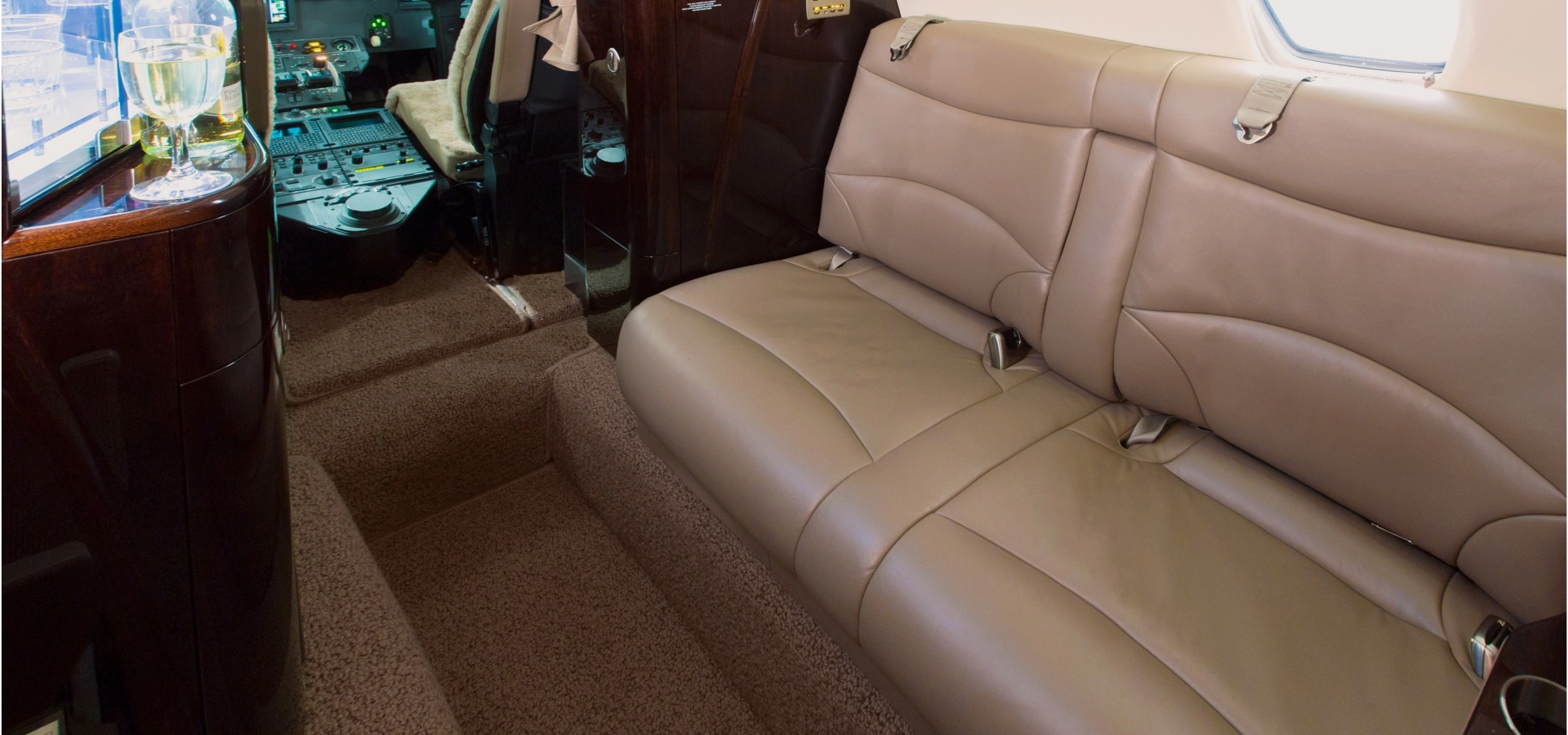 The interior of this sleek aircraft showcases beige leather seats, a small drink table on the left, and a cockpit view in the background.