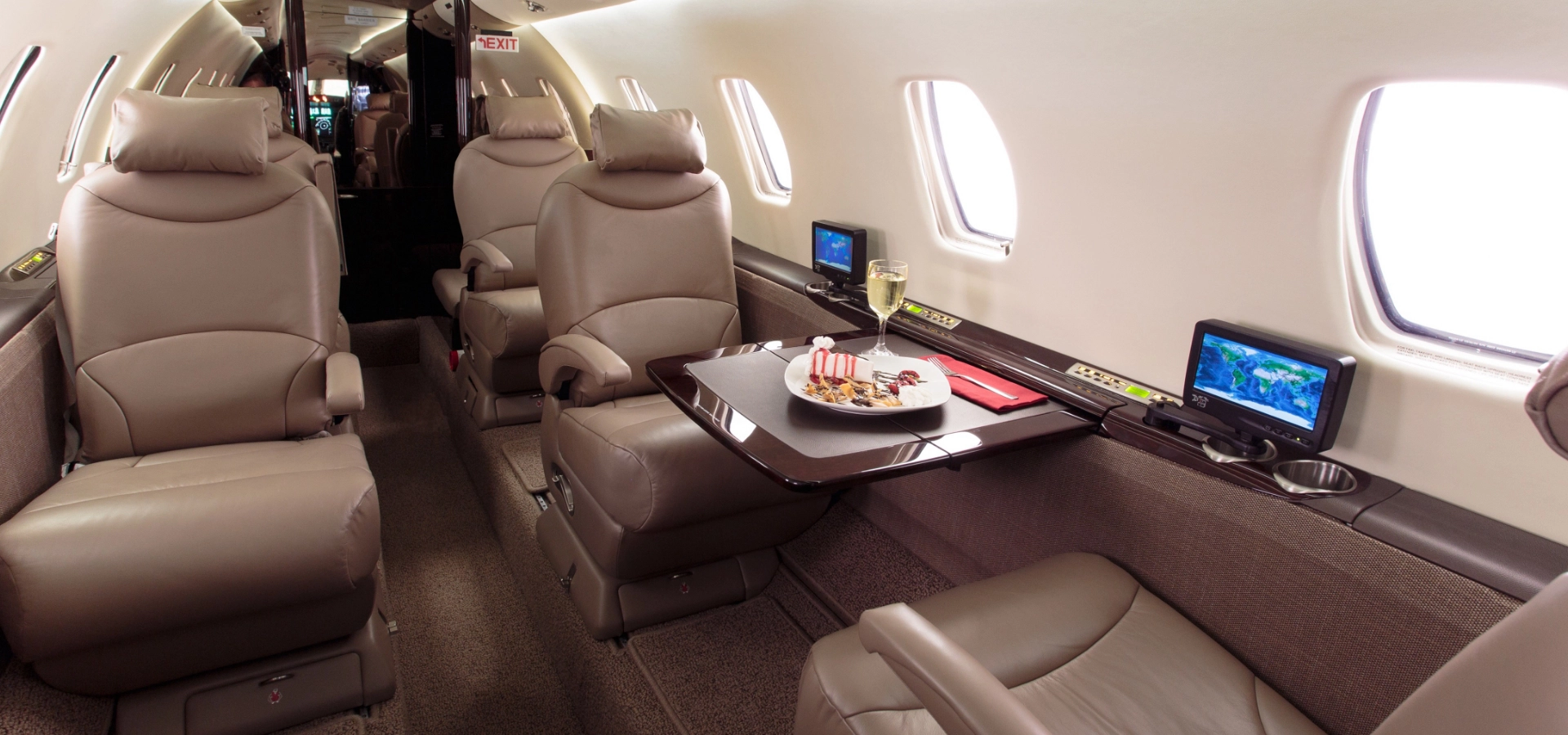 The interior of this private jet features luxurious beige leather seats, a table elegantly set with food and drink, and mounted screens.