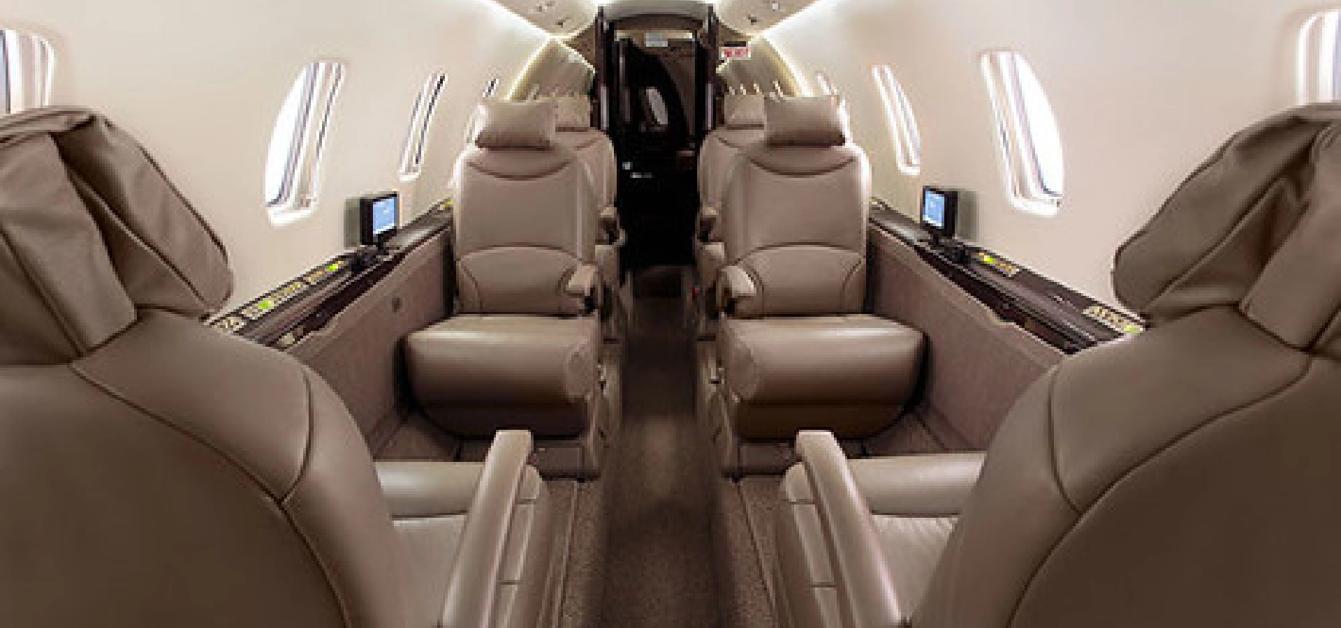The interior of a private jet, perfect for those interested in corporate jet sales, showcases luxurious leather seats arranged in two rows facing each other, complemented by small windows and sleek overhead lighting.