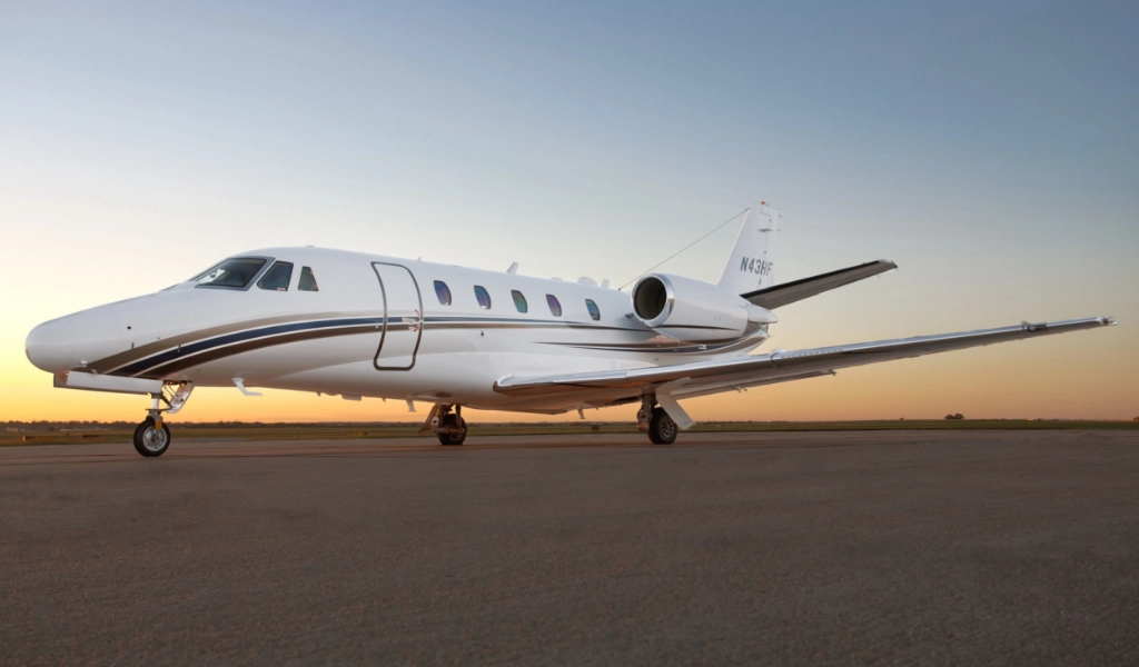 A sleek white private jet is parked on a runway with a clear sky in the background.