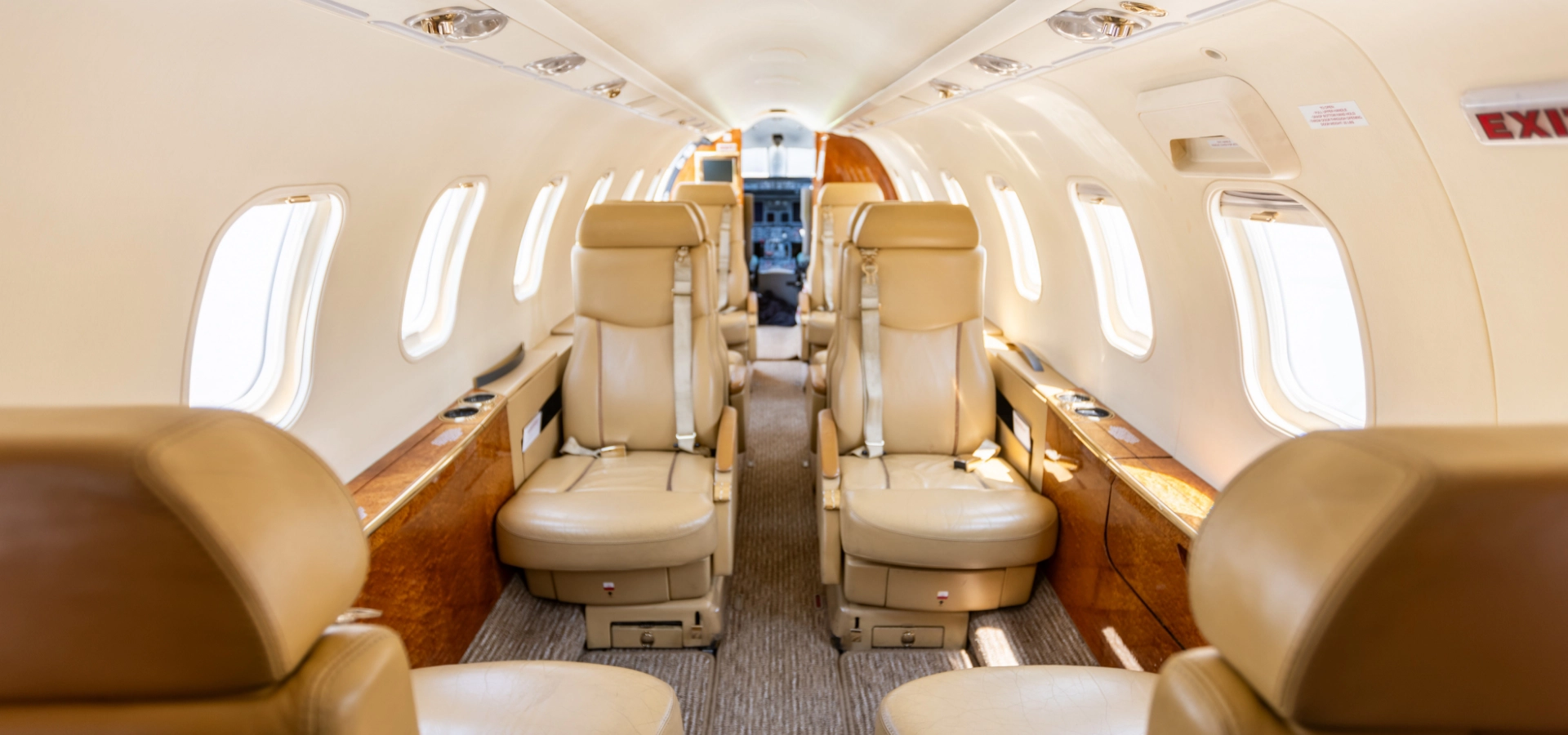 Interior of a private jet showcasing tan leather seats and large windows on both sides. The aisle runs down the center, leading to the cockpit at the front. Perfect for those exploring private jets for sale, this luxurious space exudes elegance and sophistication.