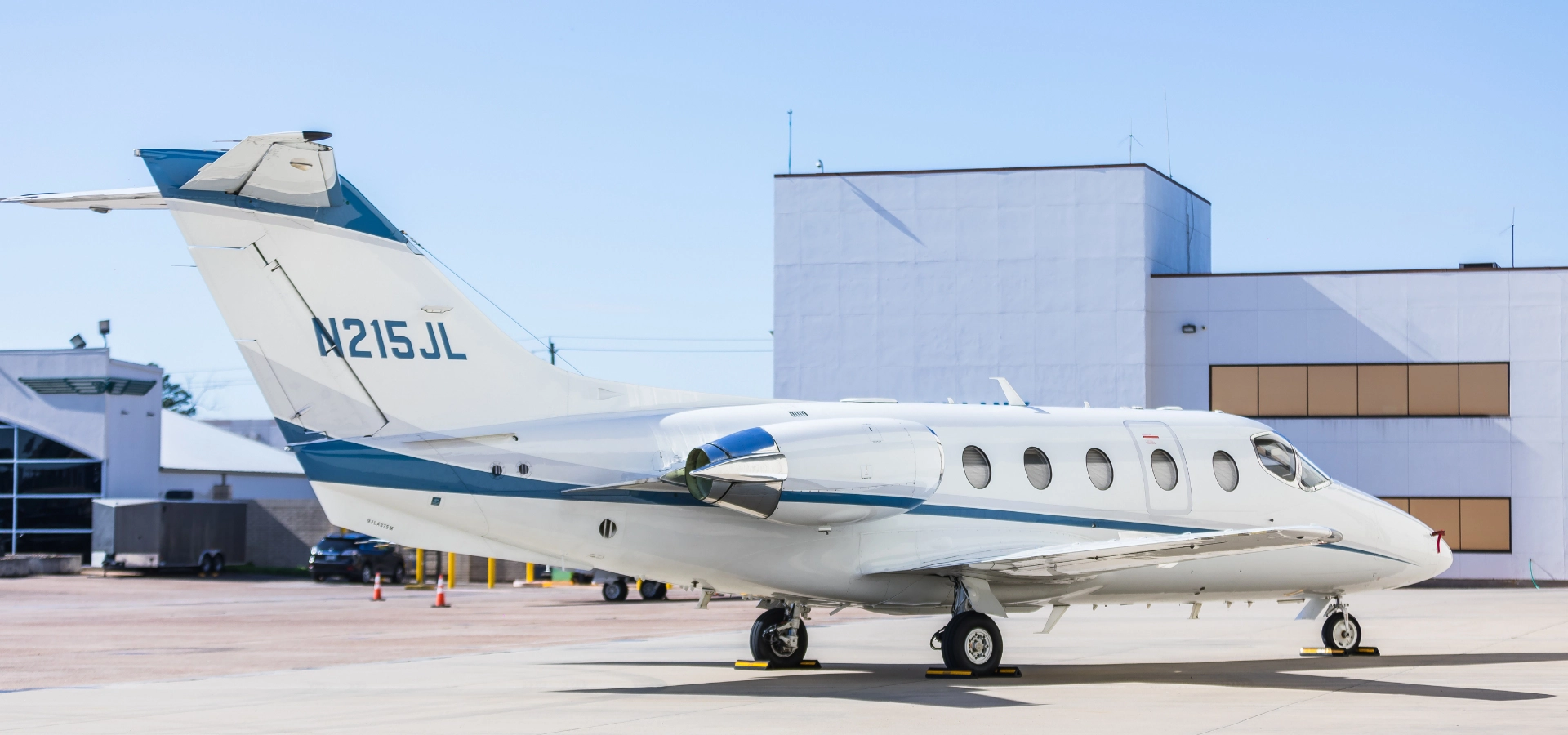 A small white and blue private jet, possibly available among luxury jet sales, is parked on a tarmac outside an airport building.