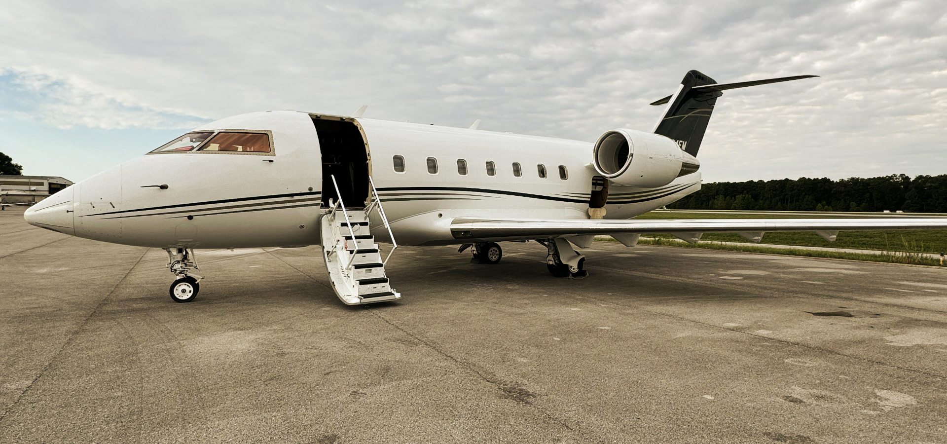A luxury jet, emblematic of elite travel, is parked on an airport tarmac with stairs gracefully extended under a partly cloudy sky.