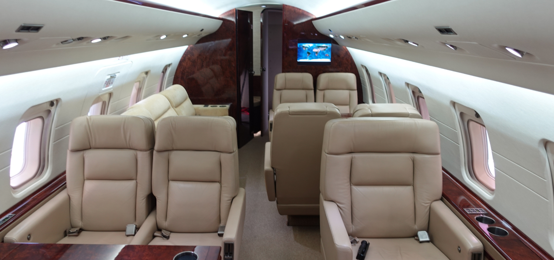 Step into the epitome of elegance with our luxury jet, featuring cream-colored leather seats, exquisite wood paneling, and a discreet screen mounted on the wall. Ideal for corporate jet sales clients seeking unparalleled comfort and sophistication in aircraft acquisition.