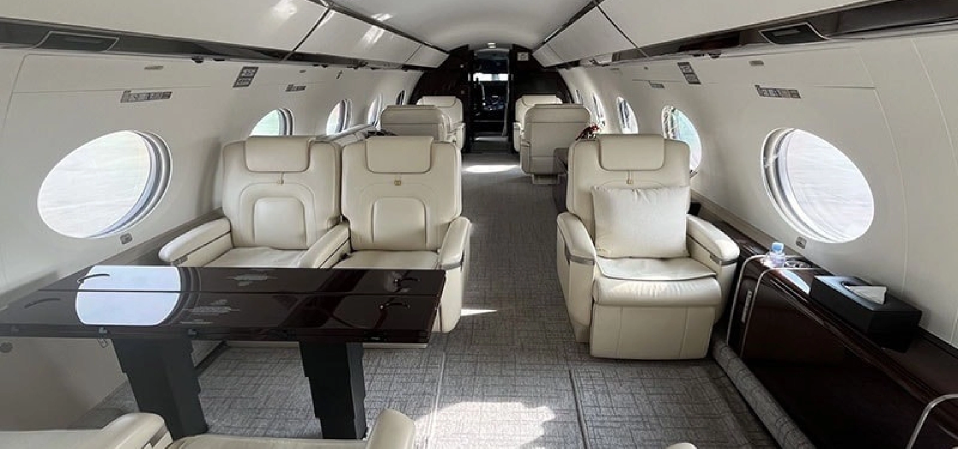 Interior view of a private jet, showcasing luxurious leather seating, a glossy wooden table, and round windows along the sides.