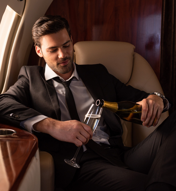 A man in a suit elegantly pours champagne into a glass while seated in a private jet, epitomizing the refined experience that comes with aircraft acquisition.