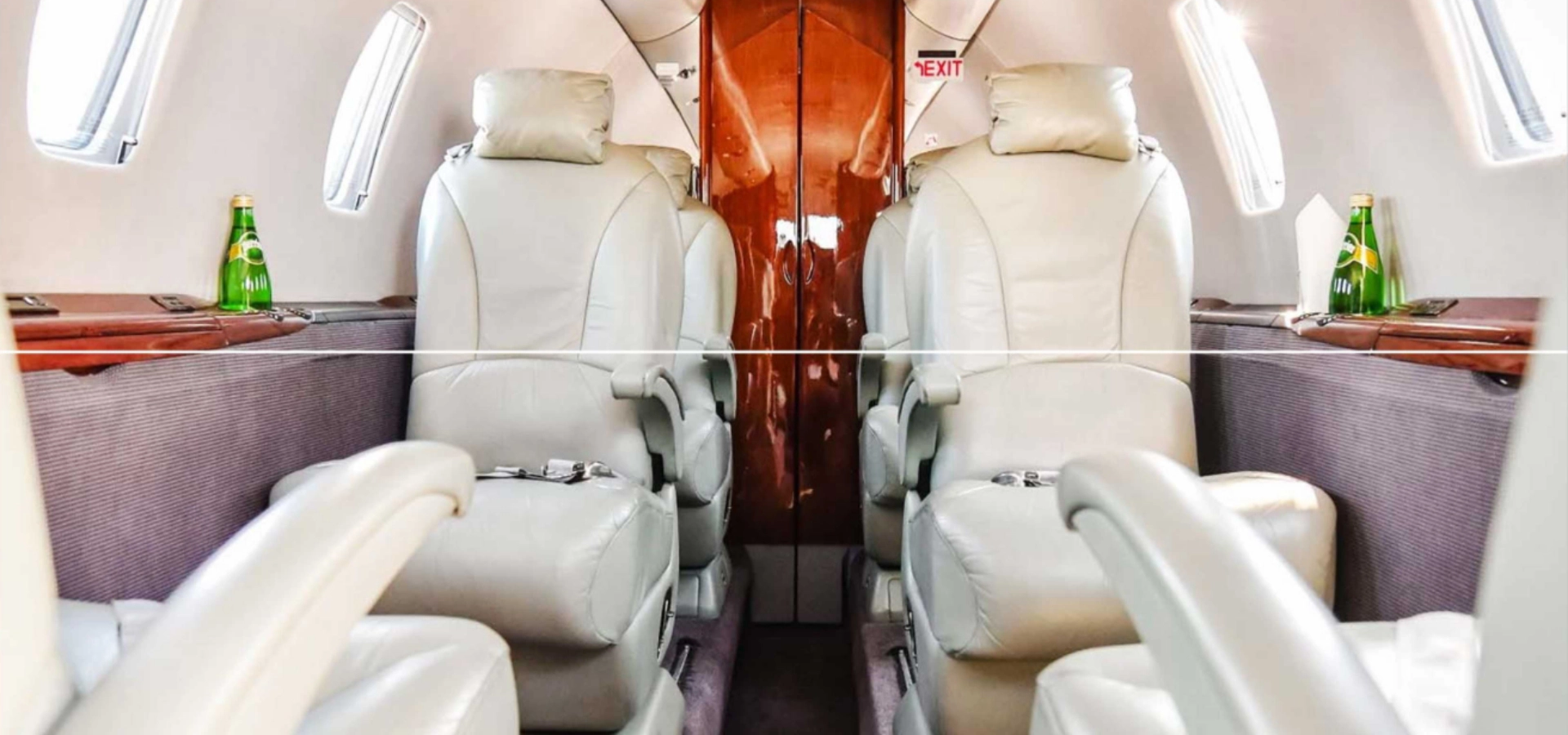 The interior of a private jet for sale features four leather seats facing each other, with elegant wood paneling. Bottled drinks rest invitingly on side tables, embodying luxury jet sales at its finest.