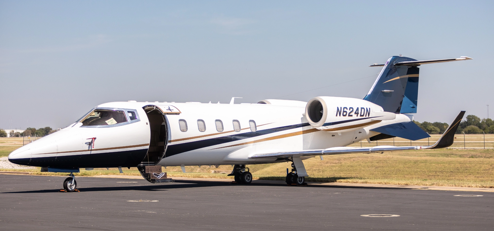 A white private jet with blue and gold accents is parked on an airport tarmac under a clear sky, a testament to elite aviation consulting services.