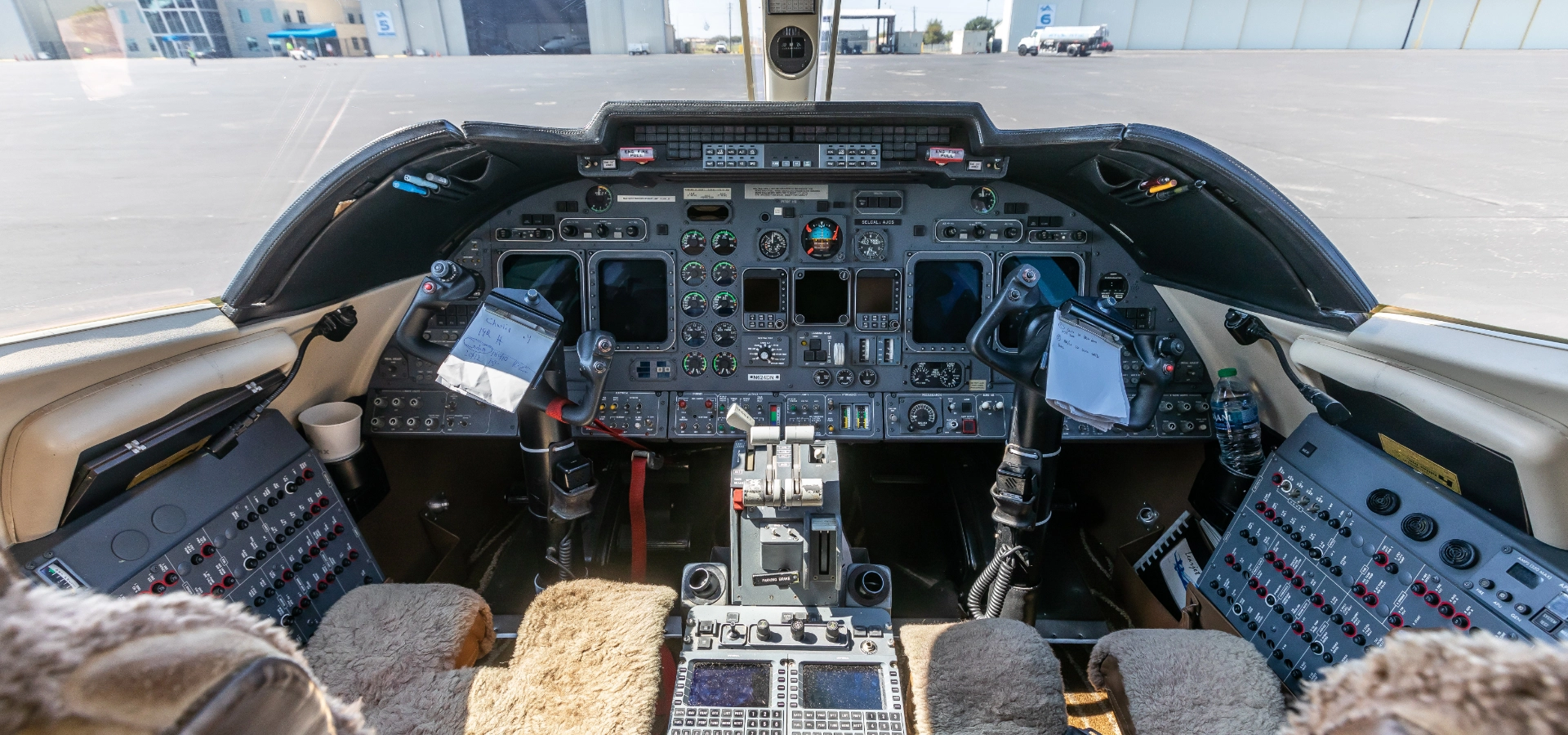 The cockpit of this corporate jet showcases a complex array of controls, switches, and displays, with two pilot seats equipped with luxurious sheepskin covers—a true testament to the sophistication found in private jets for sale.