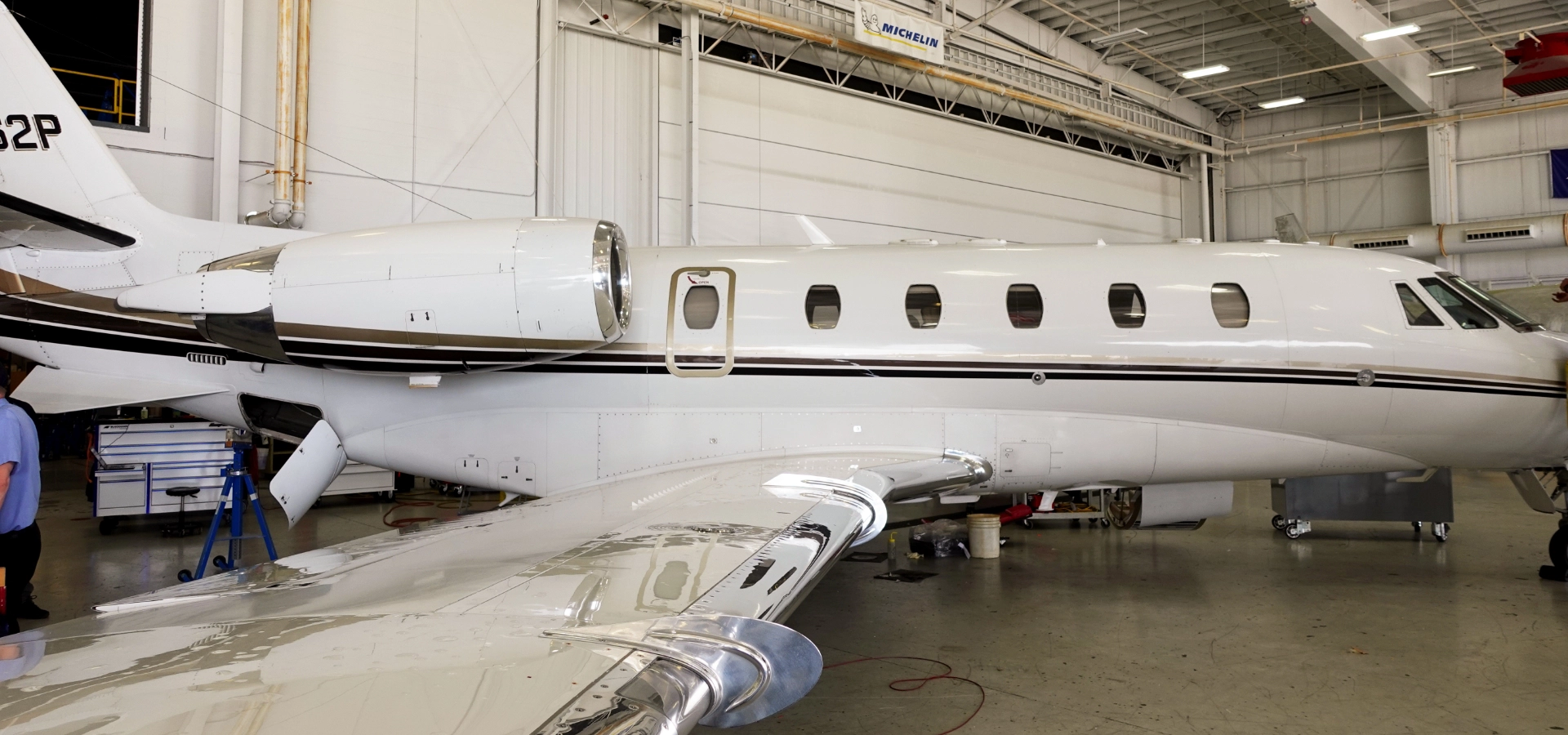 A private jet, the 2001 Citation Excel SN 5172, is parked inside an aircraft hangar. The sleek jet is white with a dark stripe along its side, exuding an aura of elegance and sophistication.