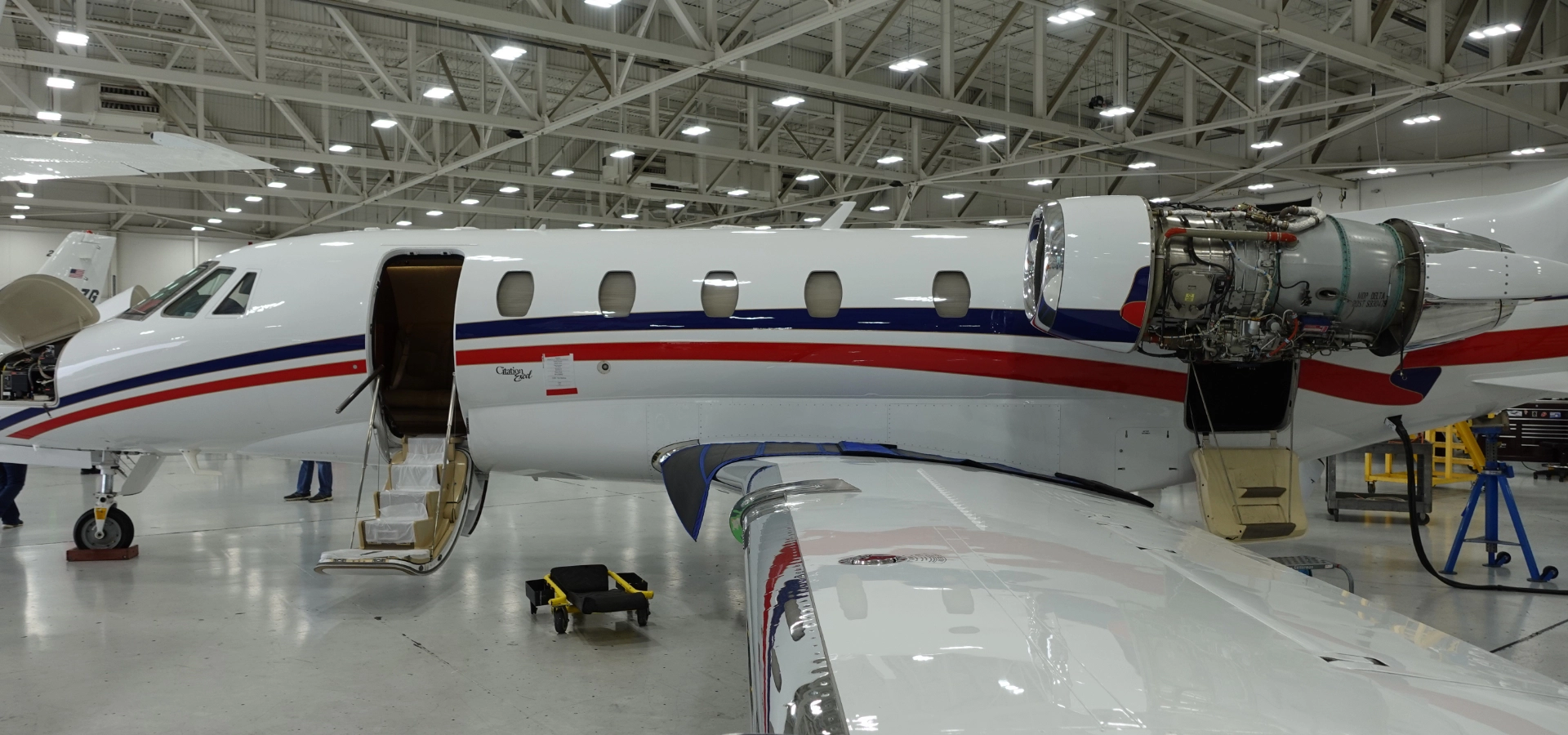 A private jet in a hangar, showcasing an open cabin door and exposed engine for maintenance, highlights the meticulous care essential for luxury jet sales.