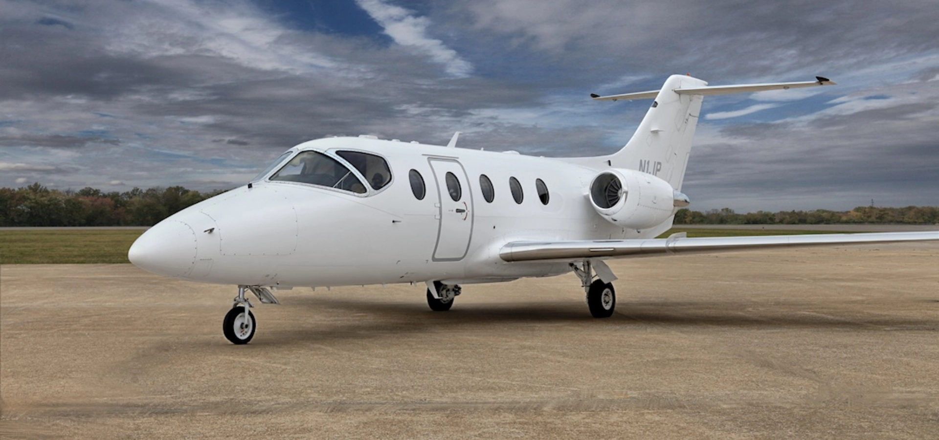 A small white private jet, reminiscent of those featured in aviation consulting services, is parked on an airfield beneath a cloudy sky.