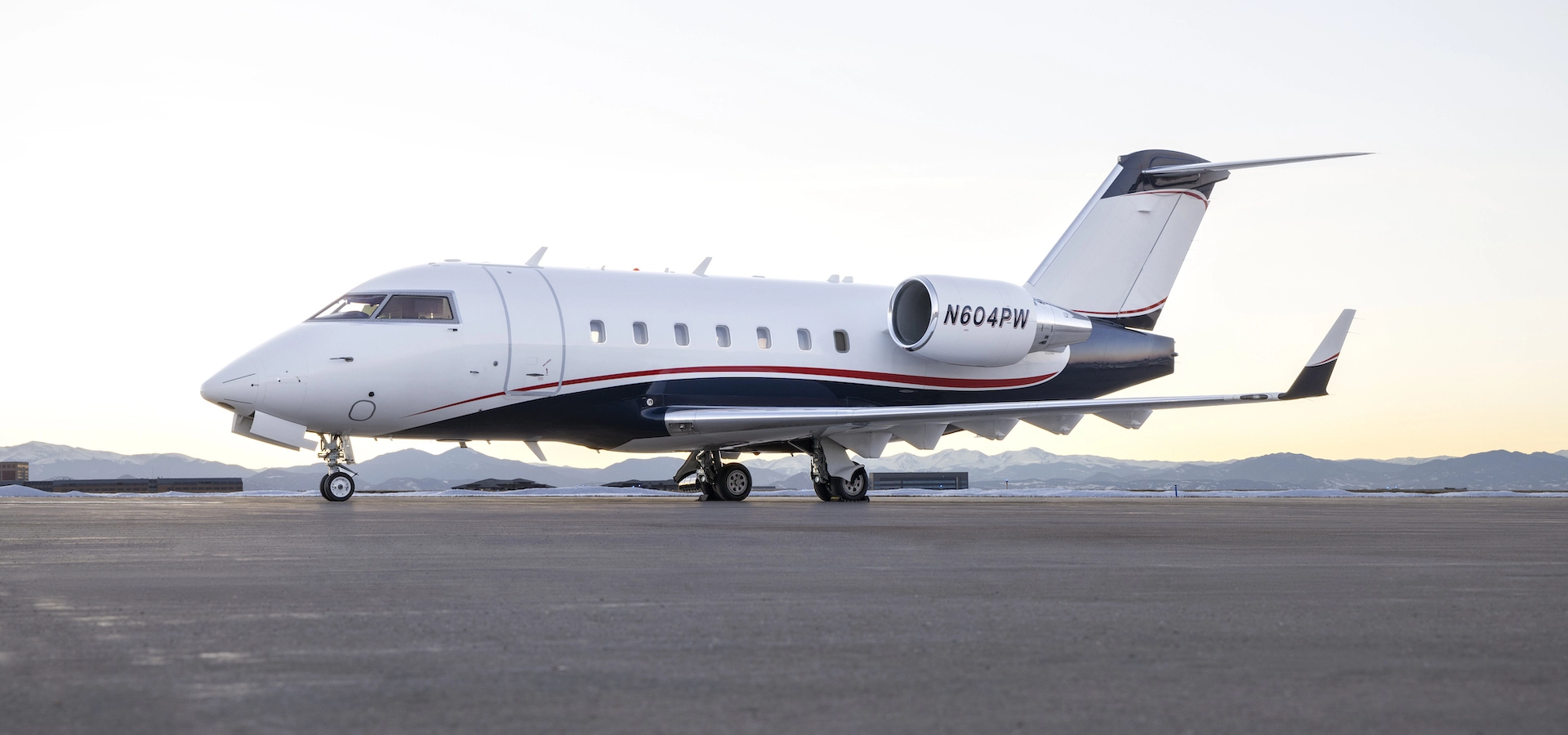 A luxury jet, available through exclusive aviation consulting services, is parked on a tarmac with mountains visible in the background at sunset.