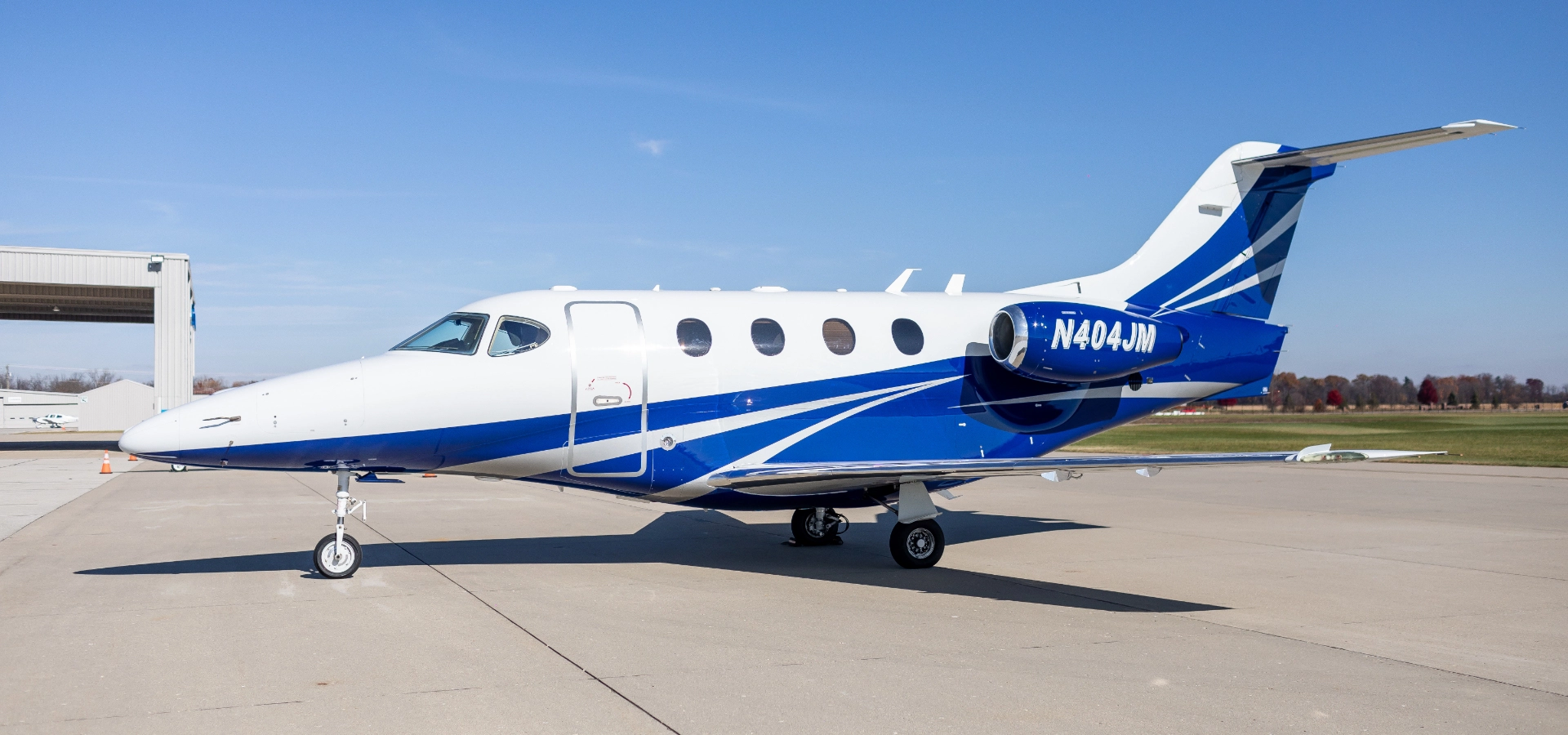 A private jet with blue and white livery, possibly available through corporate jet sales, is parked on an airport tarmac on a clear day.