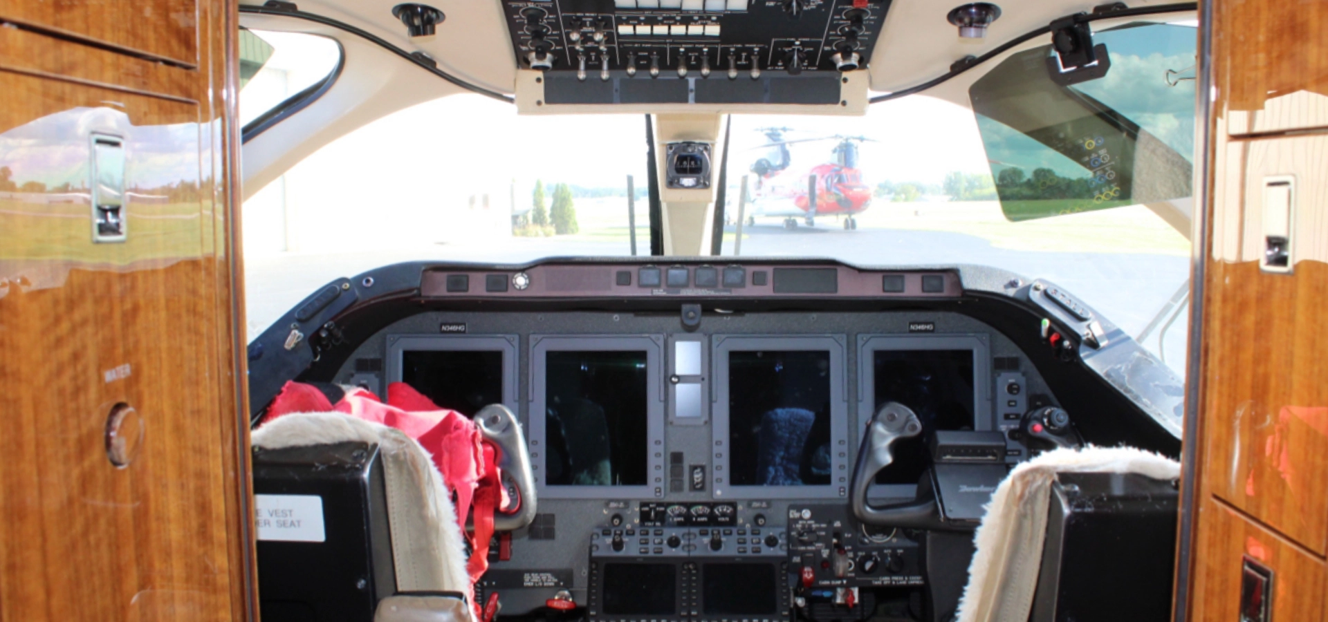 Interior view of a cockpit with multiple control panels and screens, reminiscent of luxury jet sales. A helicopter is visible outside through the windshield.