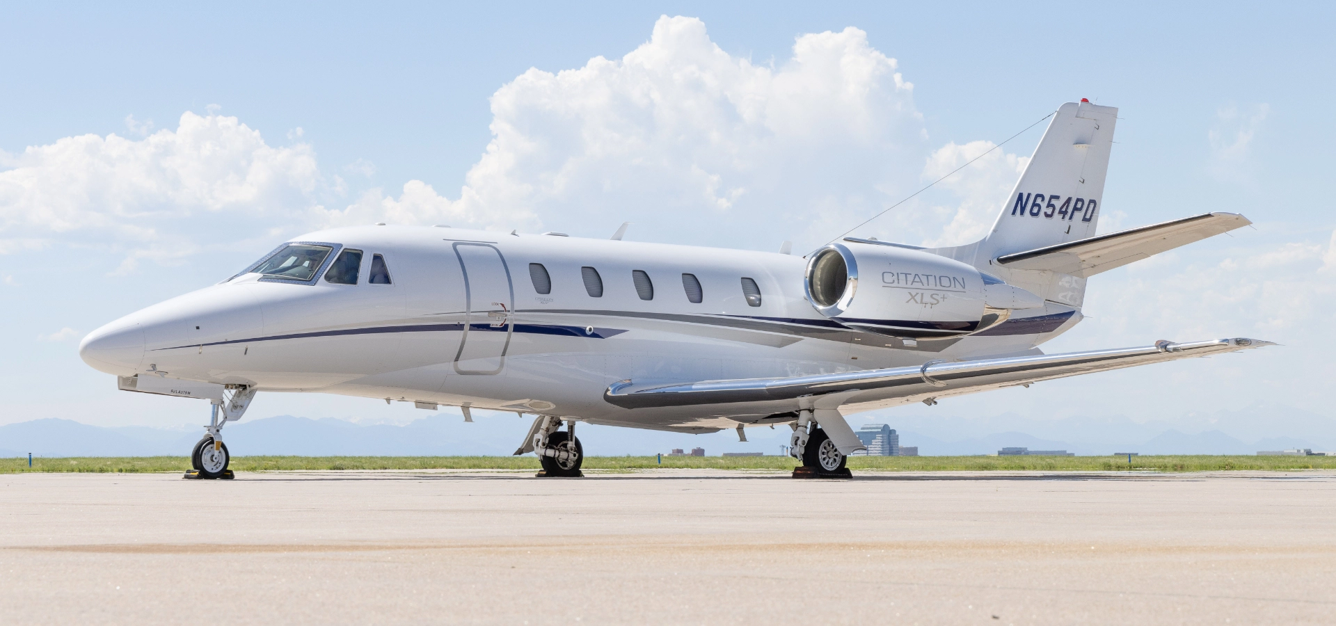 A sleek white private jet is poised against a backdrop of blue sky and distant mountains, embodying the pinnacle of luxury jet sales.