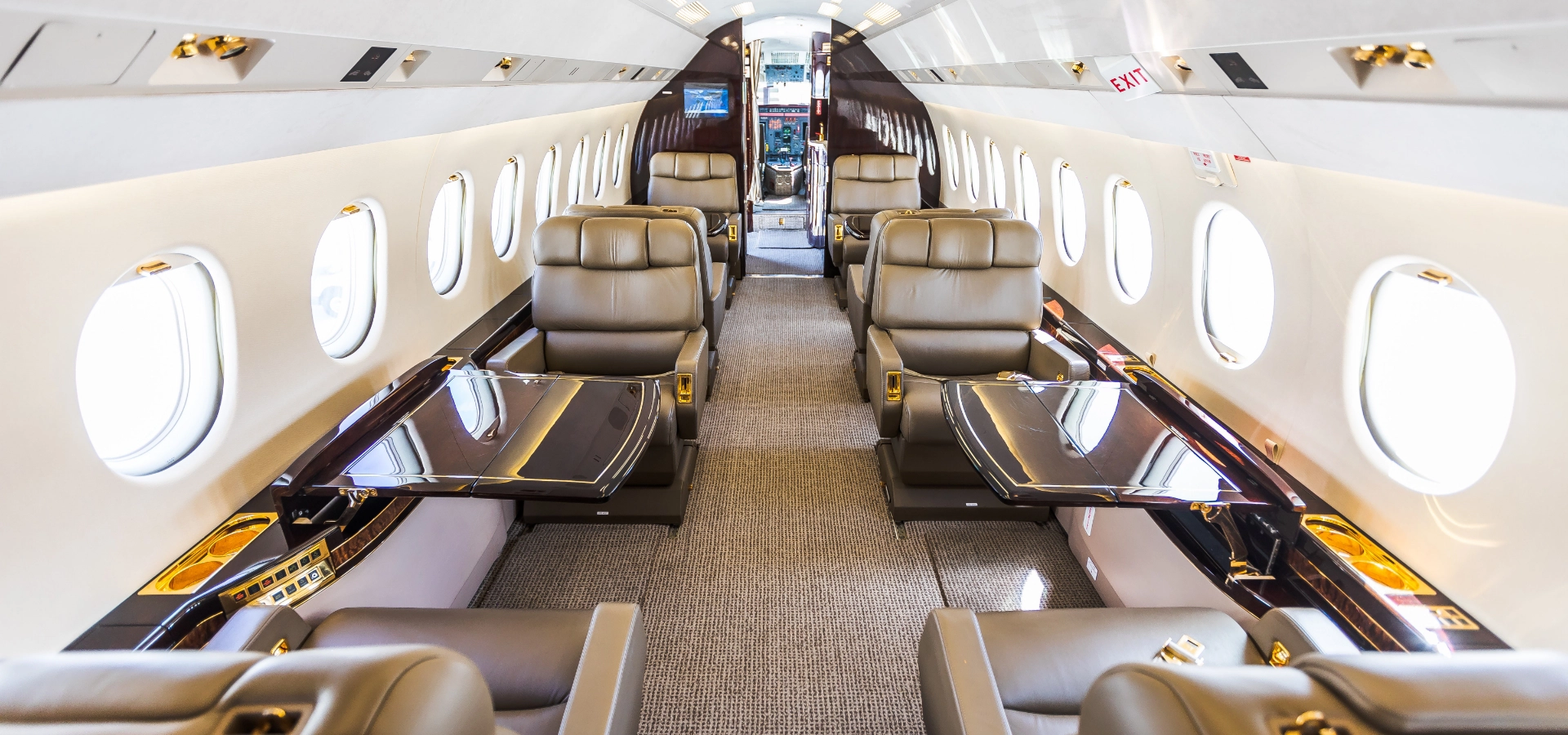 The interior of a corporate jet for sale boasts leather seating and tables, complemented by overhead storage and circular windows lining both sides.
