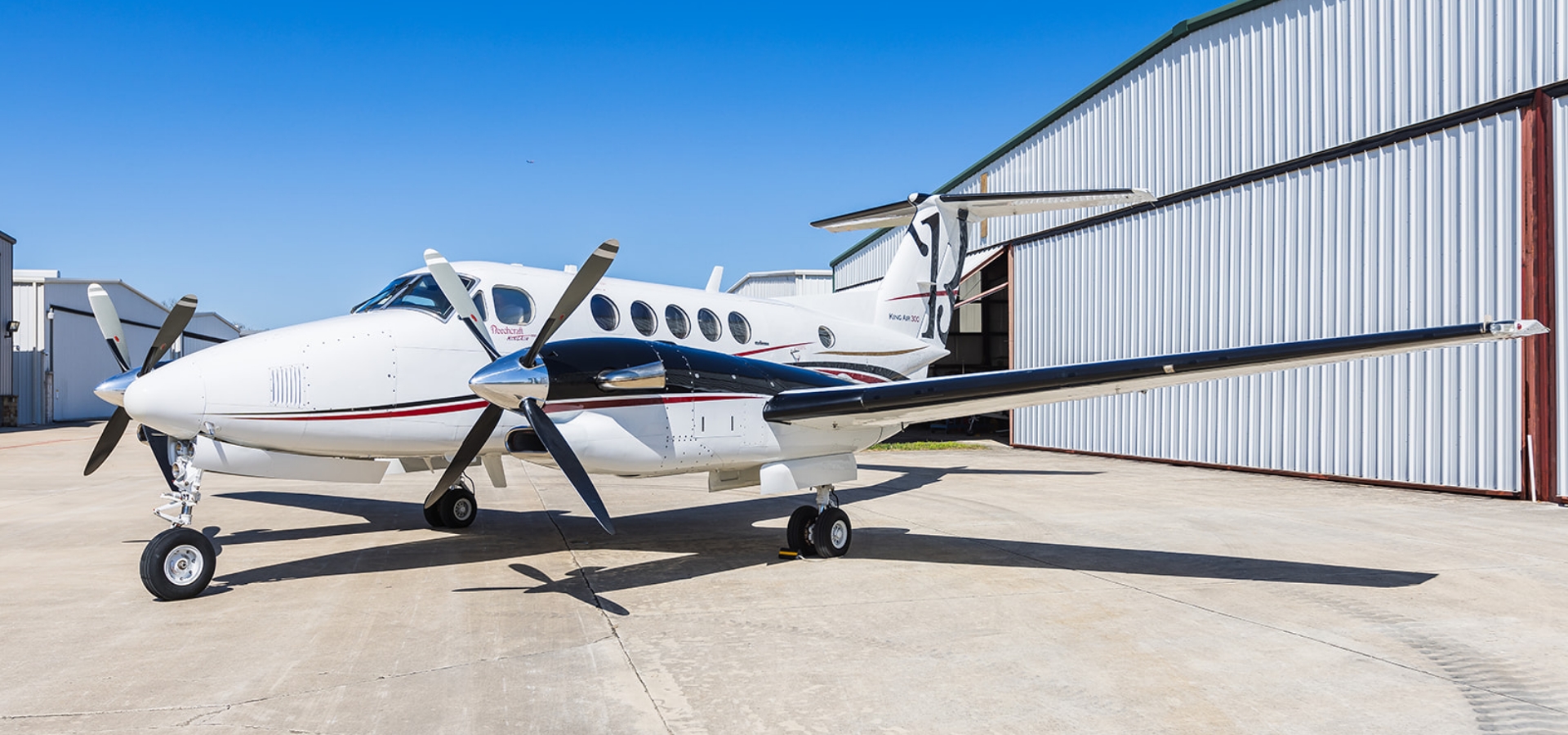 A white private propeller airplane, an ideal candidate for aircraft acquisition, is parked on the tarmac near a hangar.