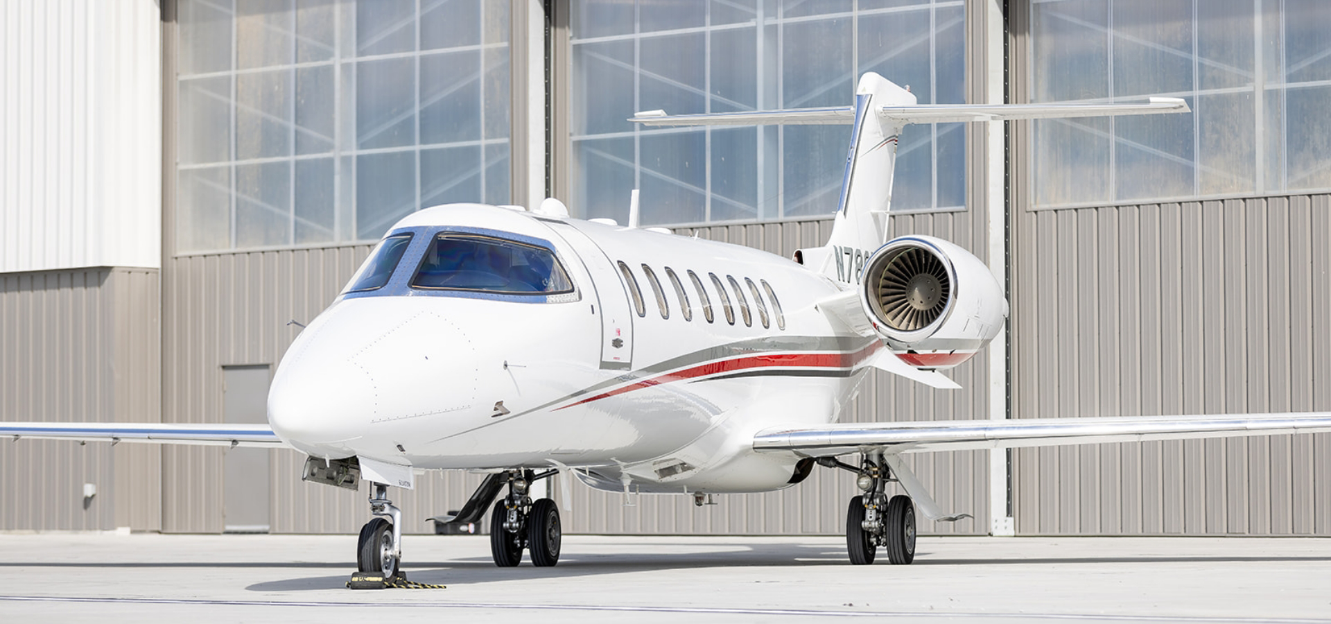 A white private jet with red and gray accents is parked in front of a large hangar, embodying the pinnacle of luxury jet sales.