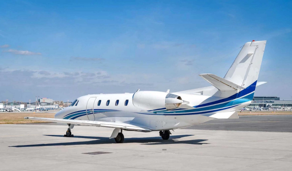 A small private jet with blue stripes, a fine example among business jets for sale, is parked on an airport tarmac under a clear blue sky.