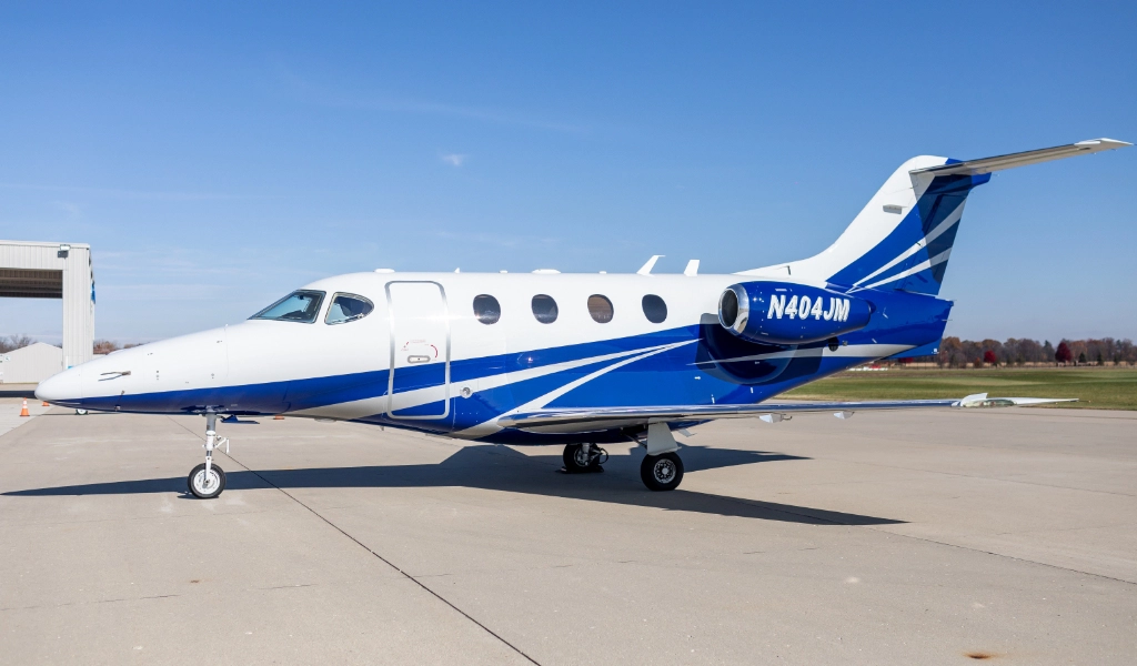 A small, blue and white private jet, emblematic of luxury jet sales, is parked on a clear day at an airport runway.