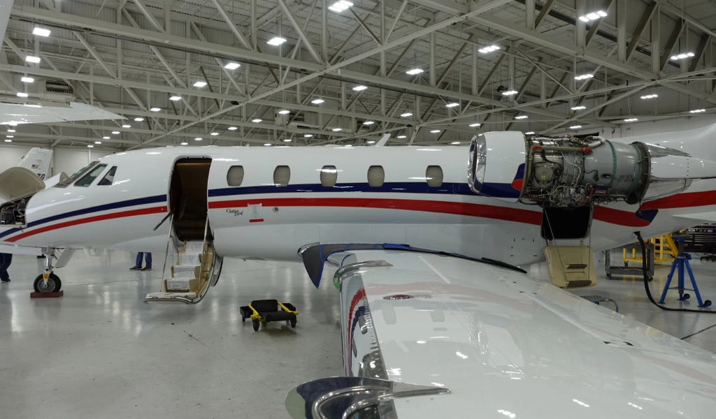 A private jet, potentially one of the luxury jets for sale, is undergoing maintenance in a hangar. Its engine cover is removed and access doors are open, offering a glimpse into its sophisticated engineering.