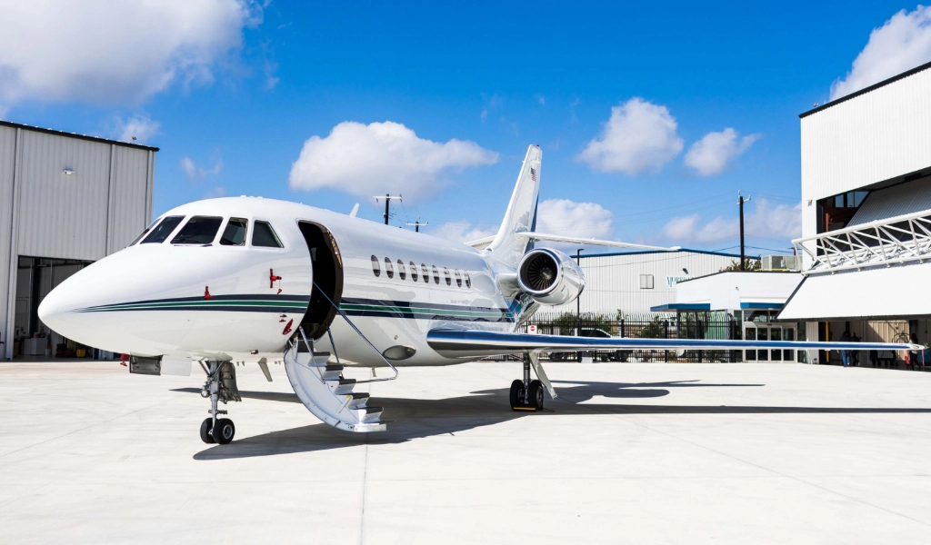 A private jet, possibly being eyed for aircraft acquisition, is parked on a clear day with visible hangars in the background. The jet's stairs are extended, inviting an inspection.