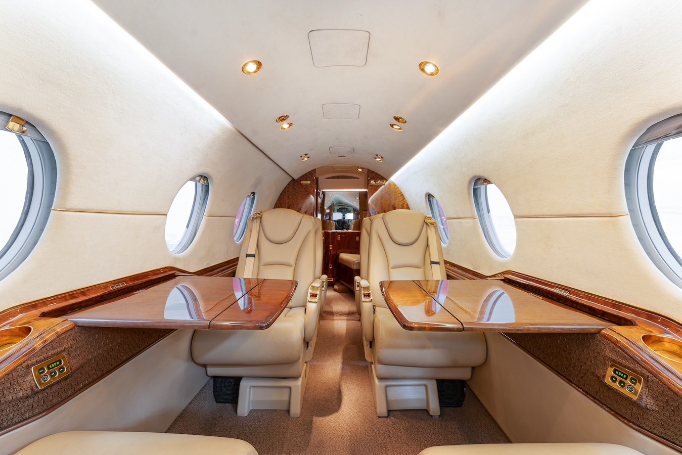The interior of a private jet exudes elegance with beige leather seats, fold-out tables, and a view of the cockpit.