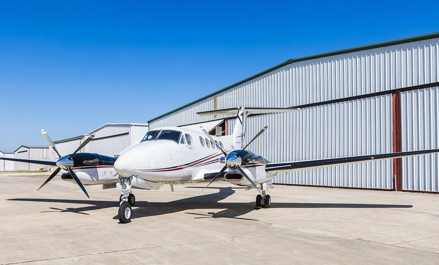 Matterhorn White with Black Velvet Metallic, Deep Red and Las Vegas Gold epitomizing luxury jet sales is parked on an airfield under a clear blue sky.
